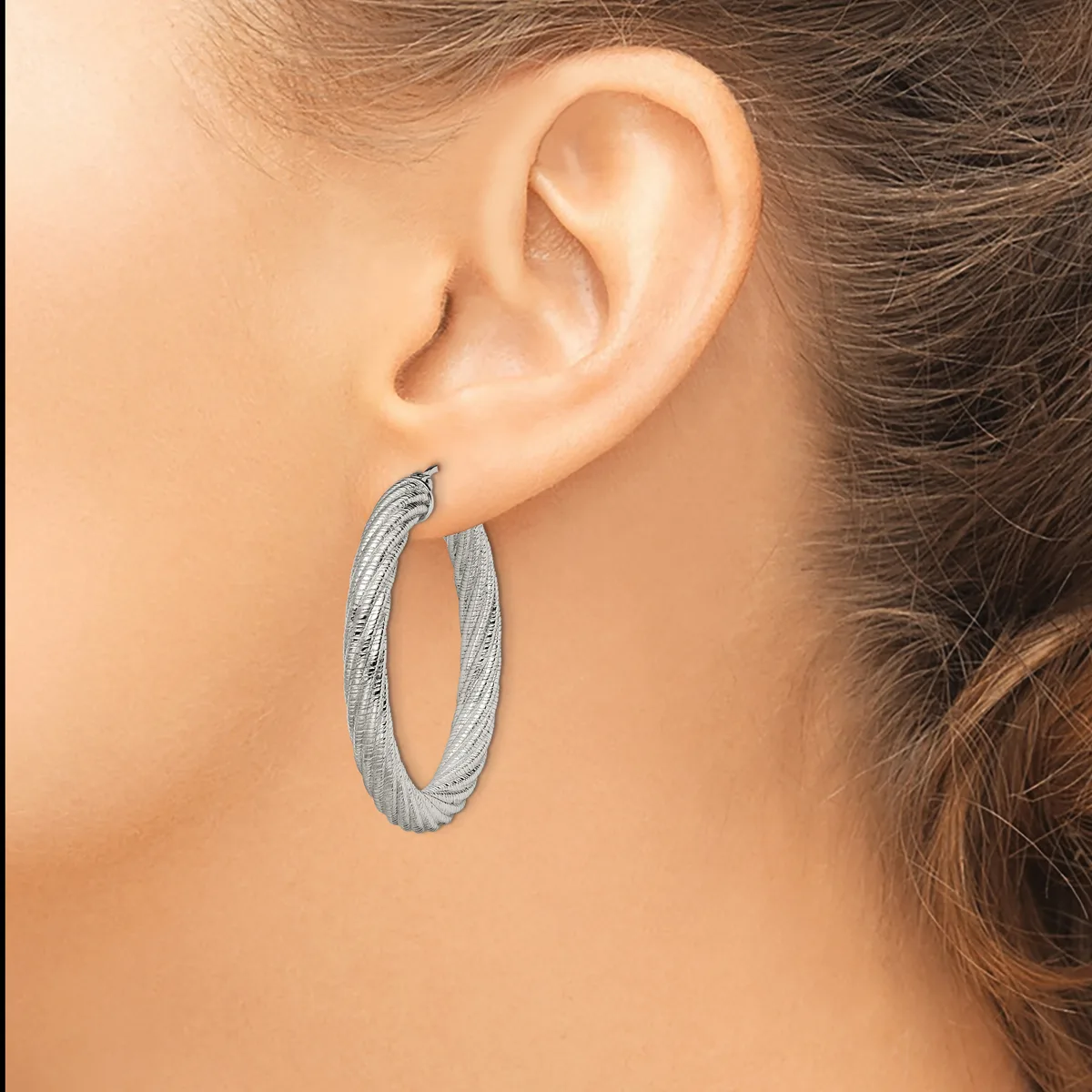 A woman wearing textured silver hoop earrings, shown from the side profile with her ear and part of her face visible.