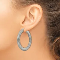 A woman wearing textured silver hoop earrings with a ridged oval design, shown from the side view against her ear.
