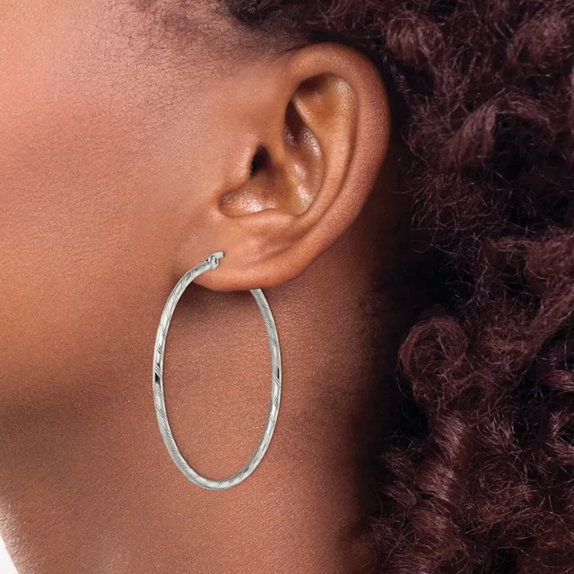 A person wearing a large oval silver hoop earring, shown in profile with their ear and dark curled hair visible.