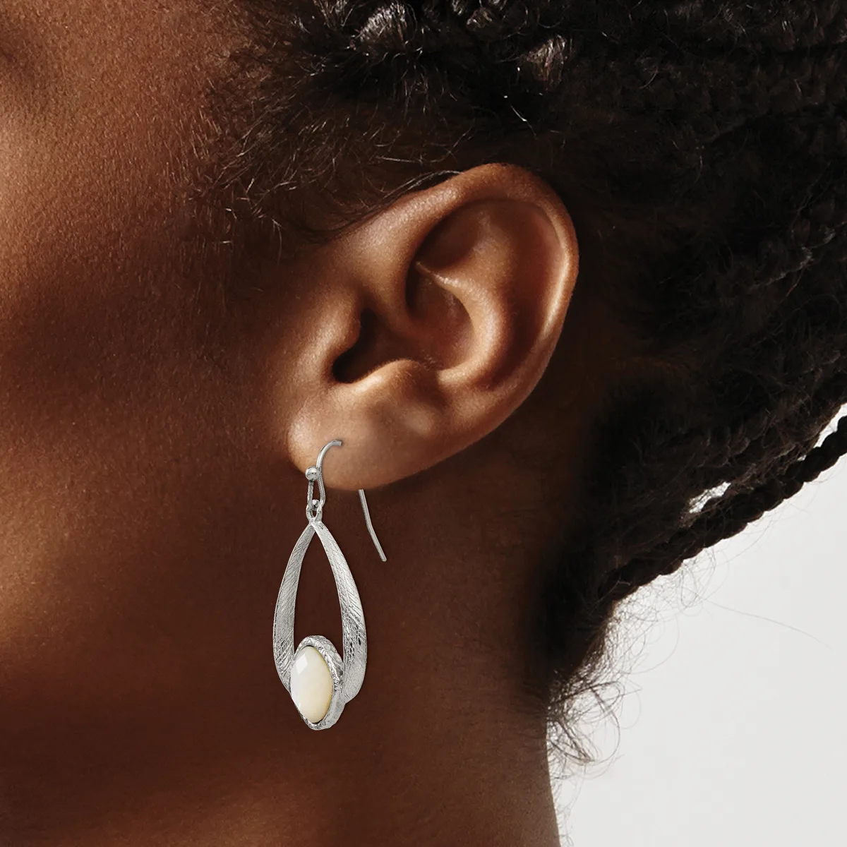 A person wearing a silver teardrop-shaped earring with a white stone or pearl accent, shown from the side view of their ear and neck.