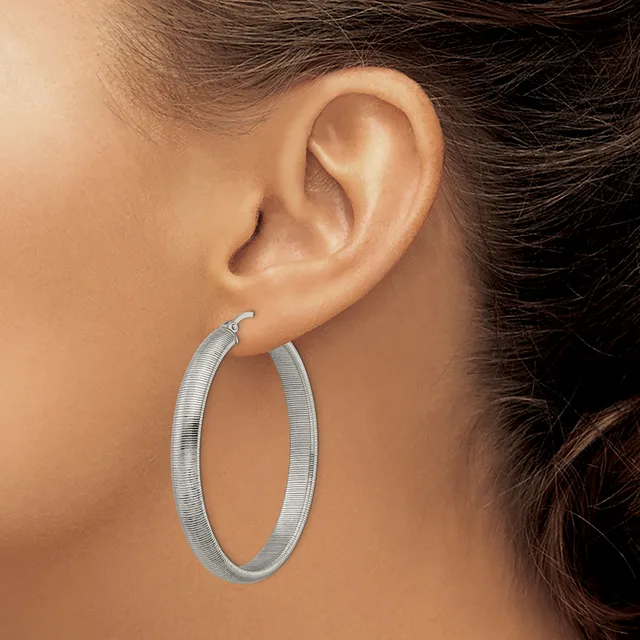 A woman wearing large oval silver hoop earrings with a textured finish, shown from the side profile with her ear and dark hair visible.