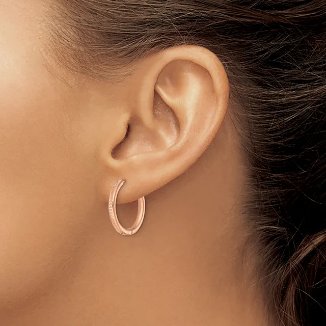 A person wearing small textured oval hoop earrings in rose gold, shown from the side profile view of their ear and neck.