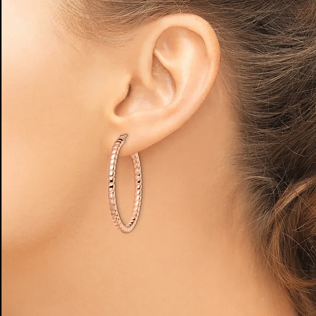 A woman wearing textured oval hoop earrings in silver-toned metal, shown from the side profile with her ear and part of her face visible.