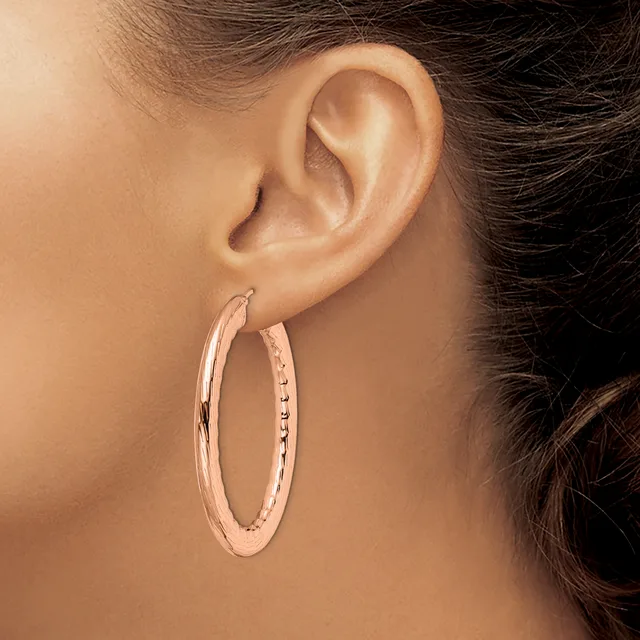 A person wearing rose gold hoop earrings with a textured surface and small gemstone accents along the inner edge.