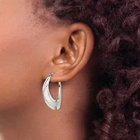 A person wearing a pair of silver hoop earrings with a decorative textured pattern, shown from the side profile against their ear.