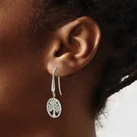 A person wearing silver drop earrings with tree of life pendants hanging from long curved wires.