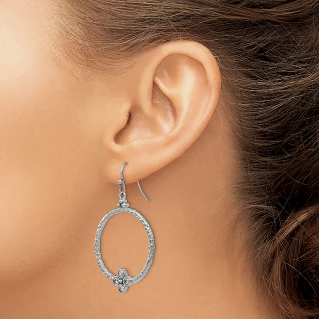 A woman wearing a silver oval-shaped dangle earring with small decorative elements at the bottom, shown from the side view of her ear.