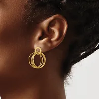 A person wearing a gold-toned circular drop earring with multiple concentric rings, shown from the side view of their ear and neck.