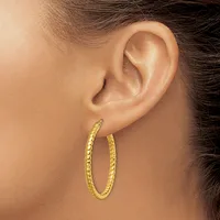 A woman wearing large gold textured hoop earrings, shown from the side with dark hair pulled back and her ear visible.