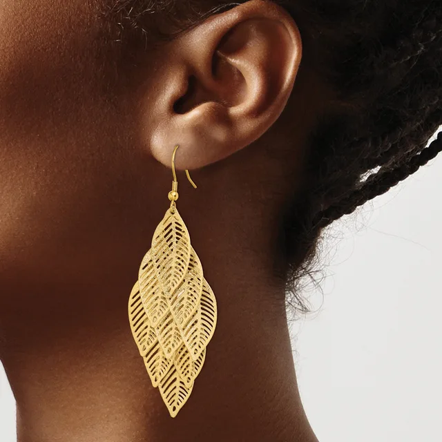 A woman wearing a gold leaf-shaped filigree earring with a fishhook closure, shown from the side against a neutral background.