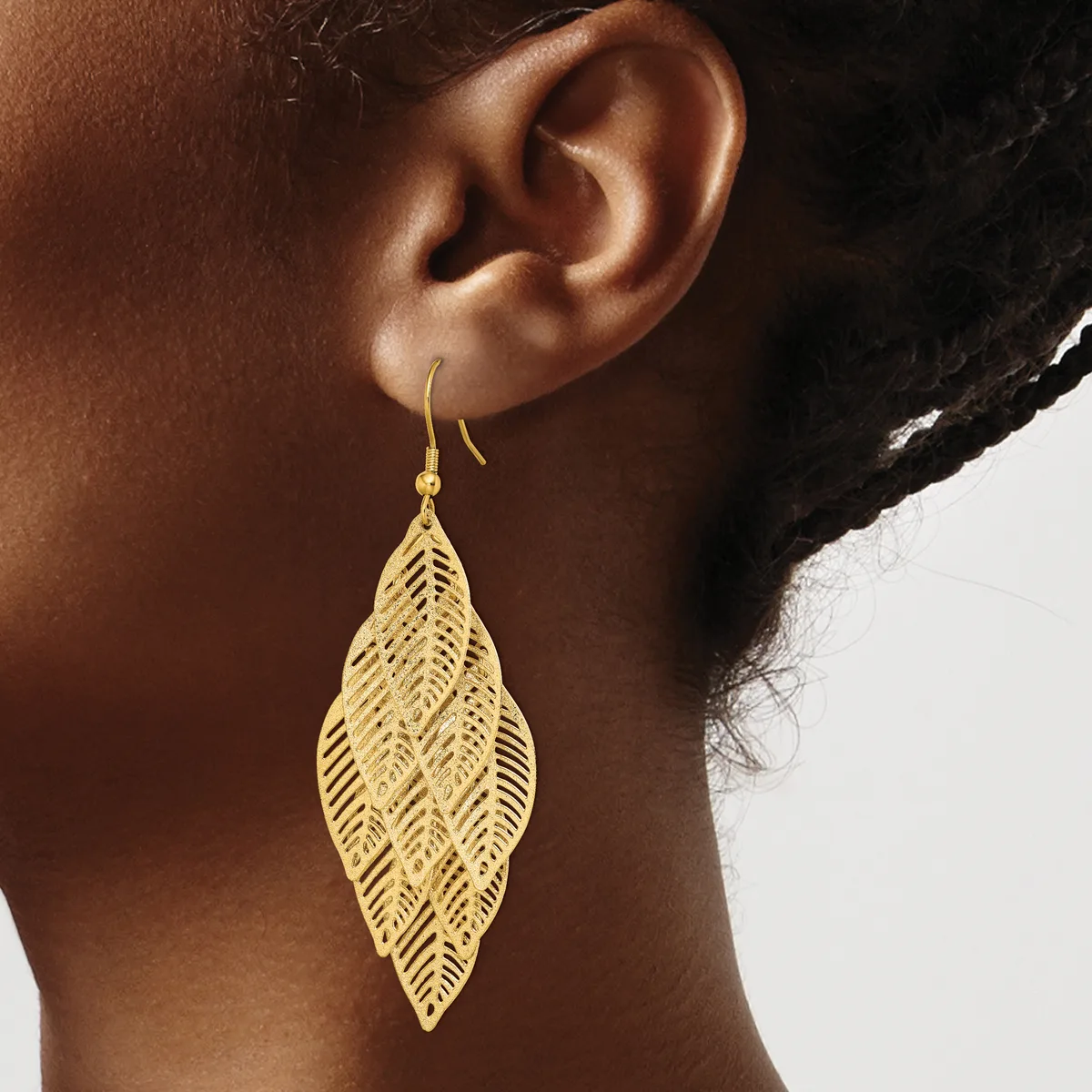 A woman wearing a gold leaf-shaped filigree earring with a fishhook closure, shown from the side against a neutral background.