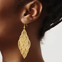 A woman wearing a gold leaf-shaped filigree earring with a fishhook closure, shown from the side against a neutral background.