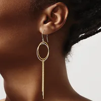 Gold-toned drop earrings with an oval loop at the top and a long chain tassel hanging below, worn by a person shown from the side.