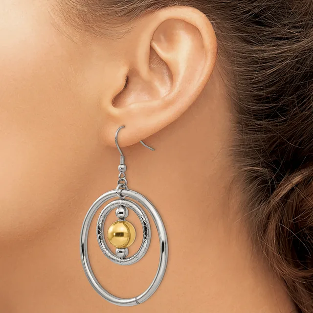 A woman wearing a dangling earring with concentric silver ovals and a gold sphere suspended in the center on a fish hook ear wire.