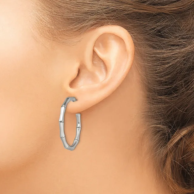 A woman wears a pair of silver hoop earrings with a segmented textured design, shown from the side view against her ear.