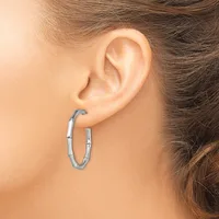 A woman wears a pair of silver hoop earrings with a segmented textured design, shown from the side view against her ear.