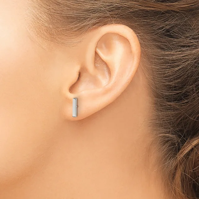 A person wearing a small rectangular silver bar stud earring in their earlobe, shown in profile view.