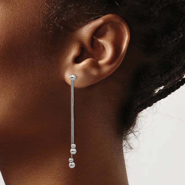 A person wearing a long silver chain earring with small beads at the end, shown from the side against a neutral background.