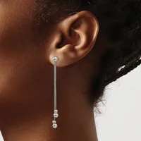 A person wearing a long silver chain earring with small beads at the end, shown from the side against a neutral background.