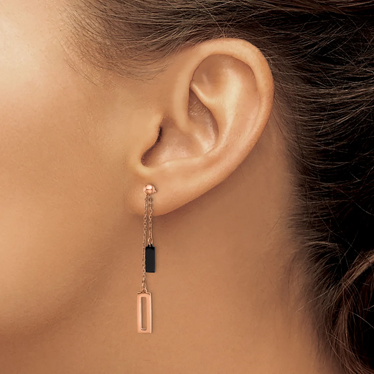 A woman wearing long dangling earrings with black and rose gold rectangular pendants connected by delicate chain links.
