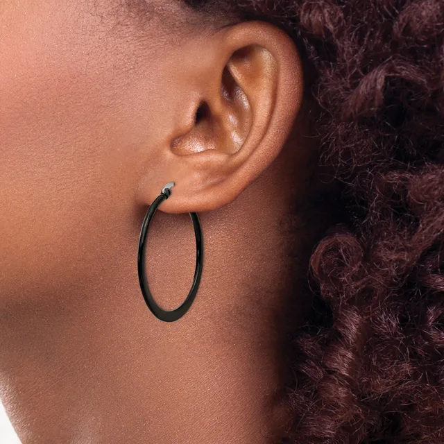A person wearing black oval hoop earrings with a small blue stone detail on the post, shown in profile against their shoulder and dark curly hair.