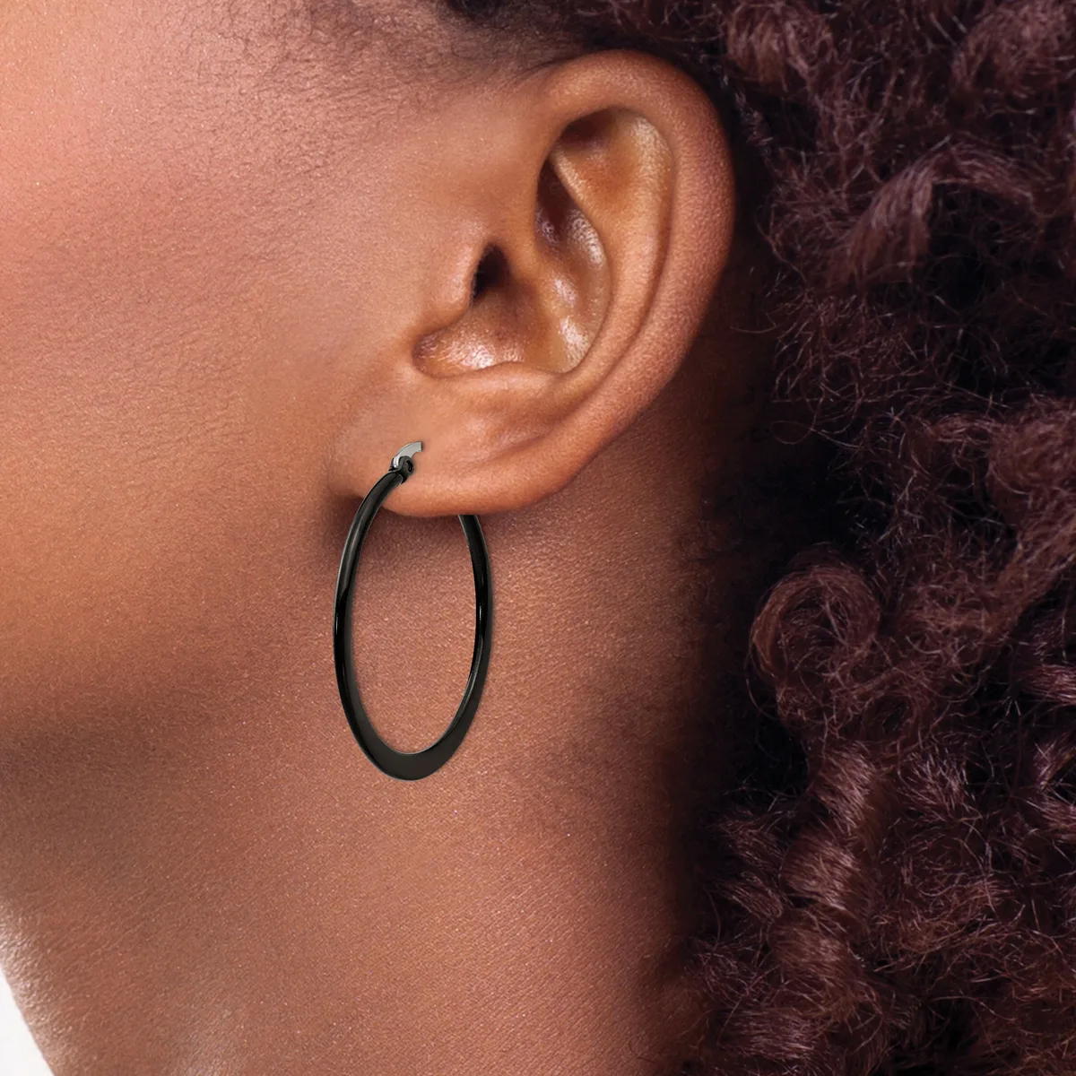 A person wearing black oval hoop earrings with a small blue stone detail on the post, shown in profile against their shoulder and dark curly hair.
