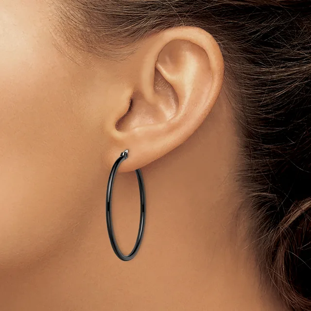 A person wearing a pair of black oval hoop earrings viewed from the side profile showing the ear and part of the face and neck.