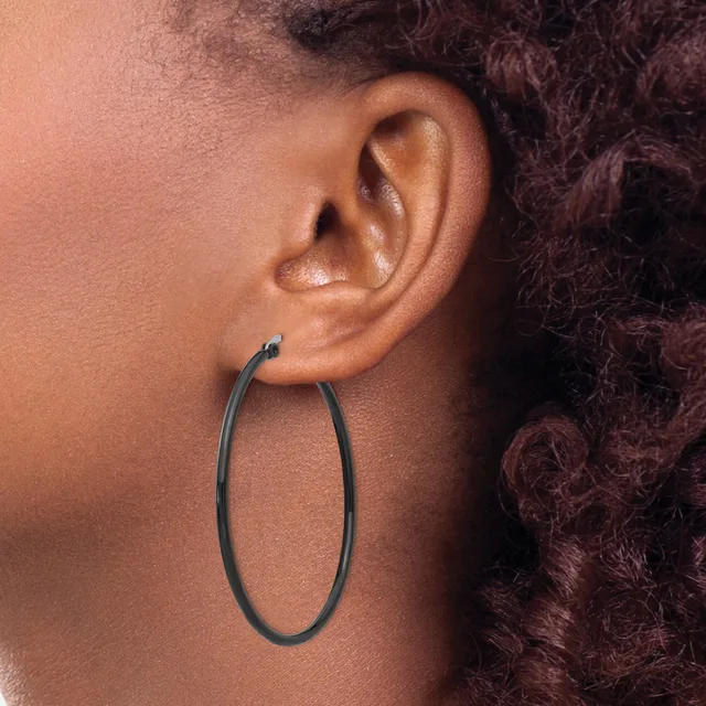 A person wearing a large oval hoop earring in dark metal, shown in profile with their ear and part of their neck and curly dark hair visible.