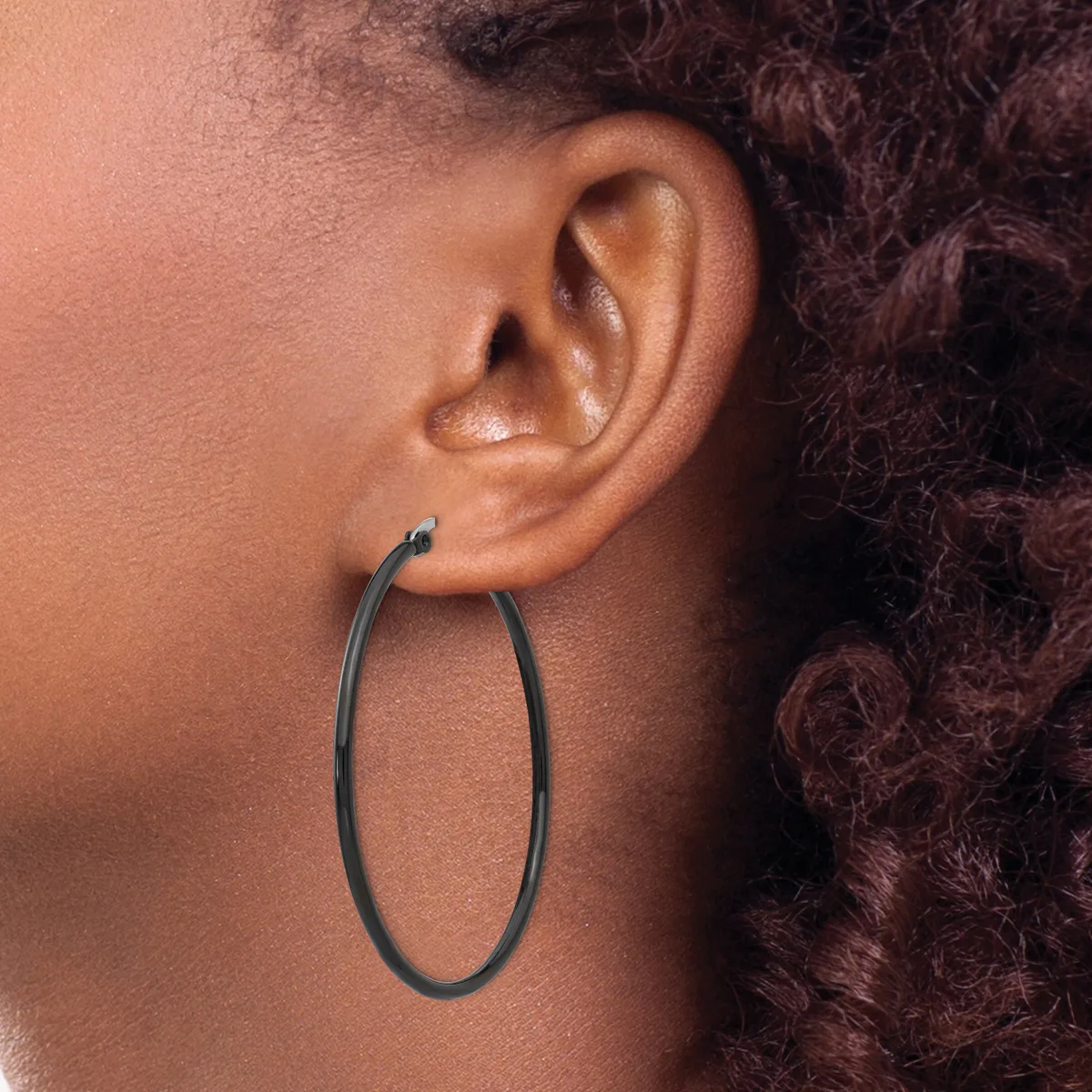 A person wearing a large oval hoop earring in dark metal, shown in profile with their ear and part of their neck and curly dark hair visible.