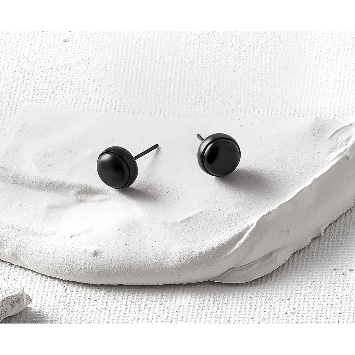 Two black spherical stud earrings with posts displayed on a white textured fabric surface.