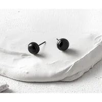 Two black spherical stud earrings with posts displayed on a white textured fabric surface.