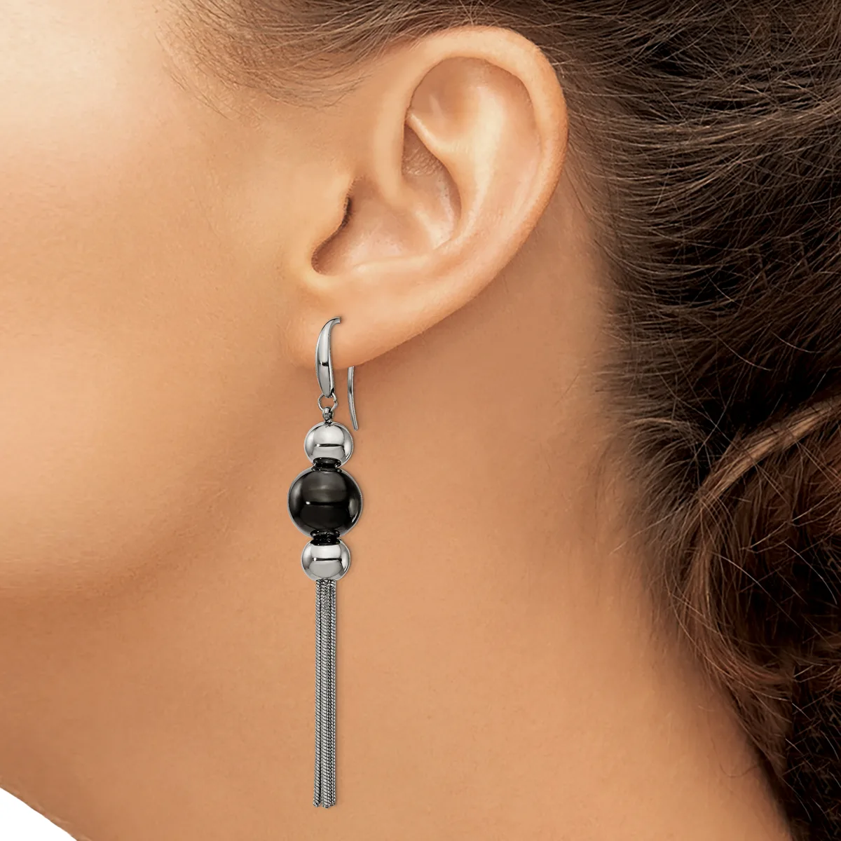 A woman wearing a dangling earring with a black sphere bead between two silver spheres and a long tassel chain hanging from a lever-back hook.