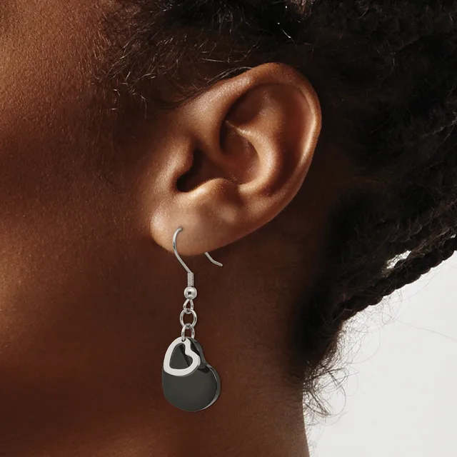 A person wearing a silver fish hook earring with a chain and black circular pendant hanging from their earlobe.