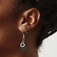 A person wearing a silver fish hook earring with a chain and black circular pendant hanging from their earlobe.