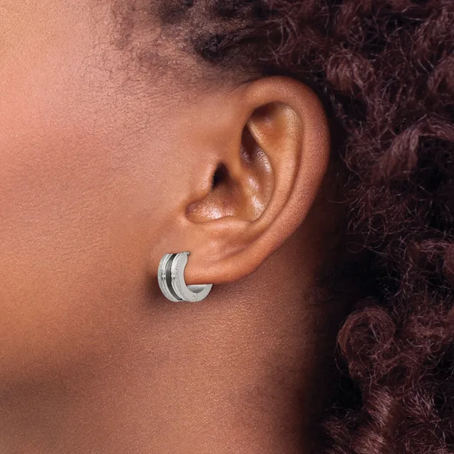 A person wearing a silver curved hoop earring with a textured center stripe, shown from the side profile against their ear and dark curly hair.