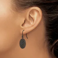 A person wearing a pair of dark metal oval dangle earrings with a textured surface on curved ear wires.