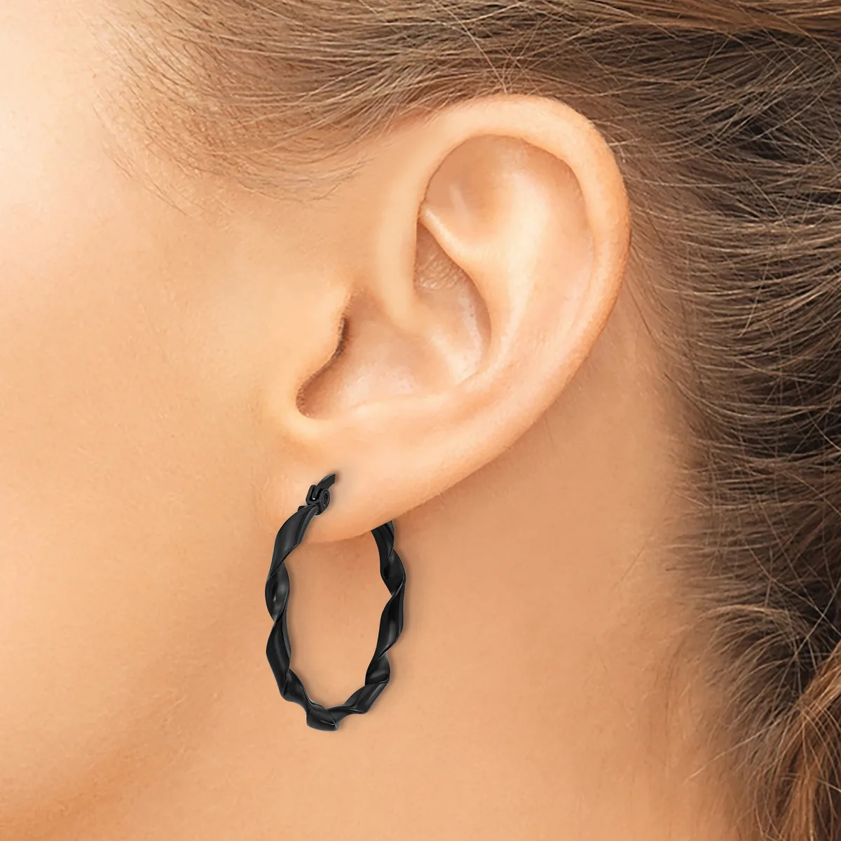 A person wearing a pair of black twisted hoop earrings, shown from the side profile of their head and ear.