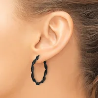 A person wearing a pair of black twisted hoop earrings, shown from the side profile of their head and ear.
