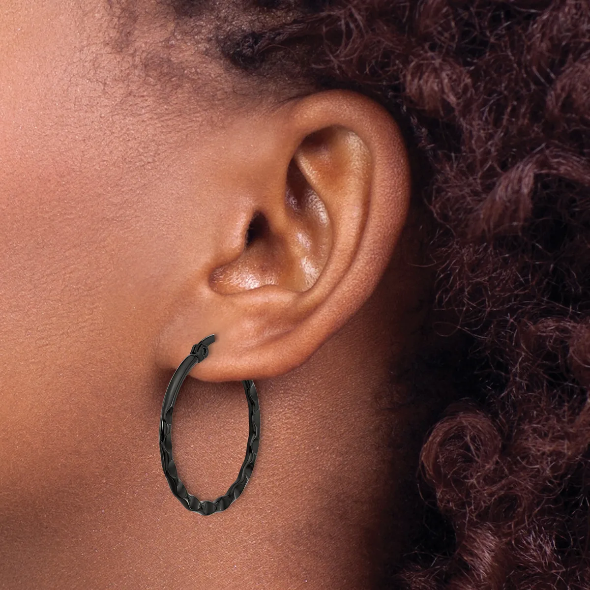 A person wearing a black textured hoop earring in their earlobe, shown in profile against their skin.