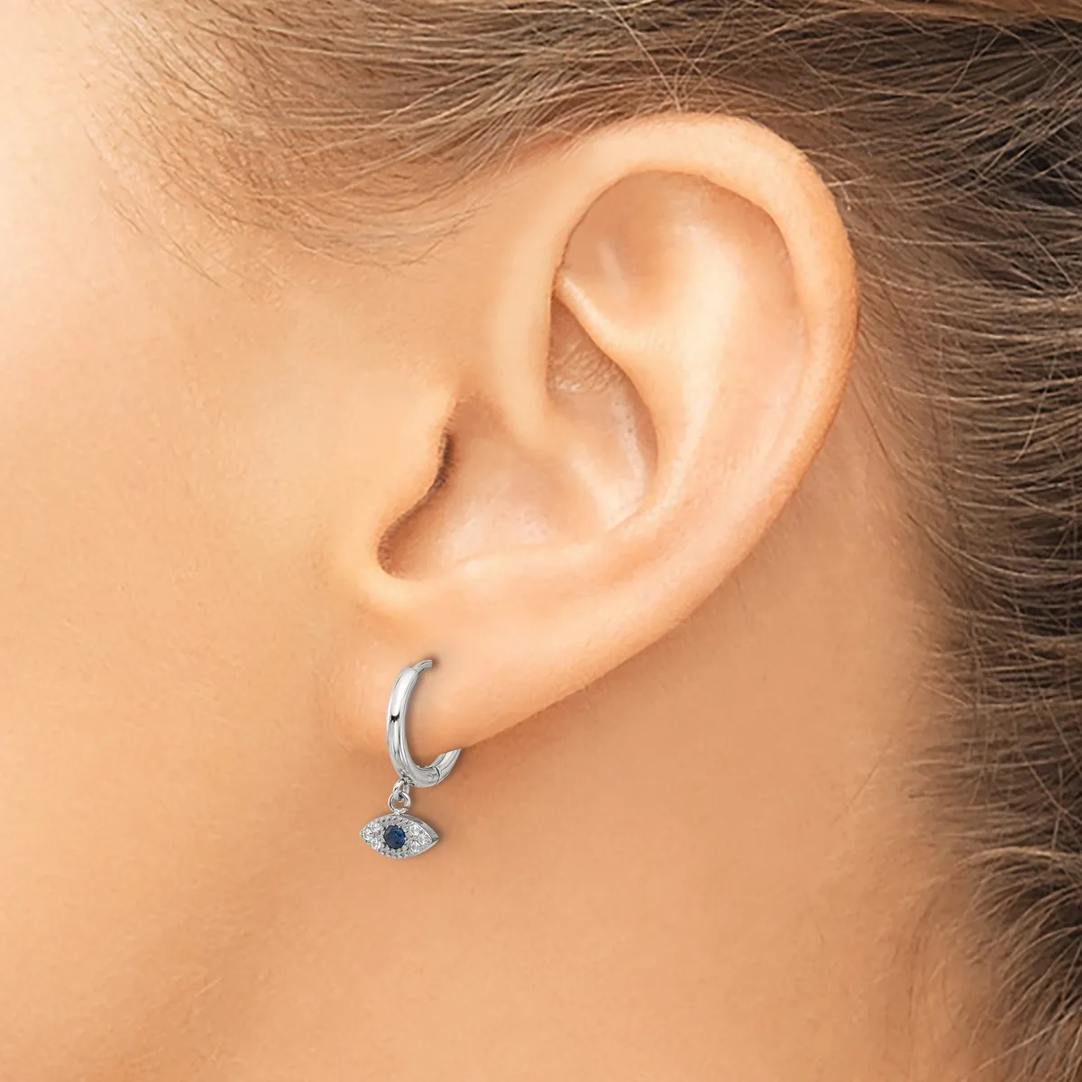 A person wearing a silver hoop earring with a small dangling pendant featuring a dark blue stone surrounded by smaller crystals.