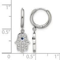 A pair of silver huggie hoop earrings with hamsa hand charms featuring white crystals and a blue stone center, shown next to a ruler for scale.