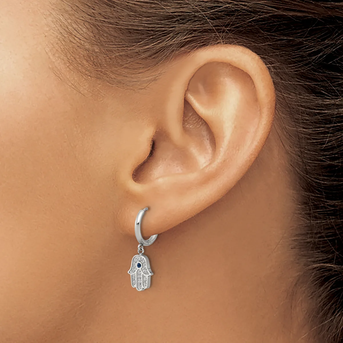 A person wearing a silver hoop earring with a dangling hamsa hand charm, shown from the side profile.