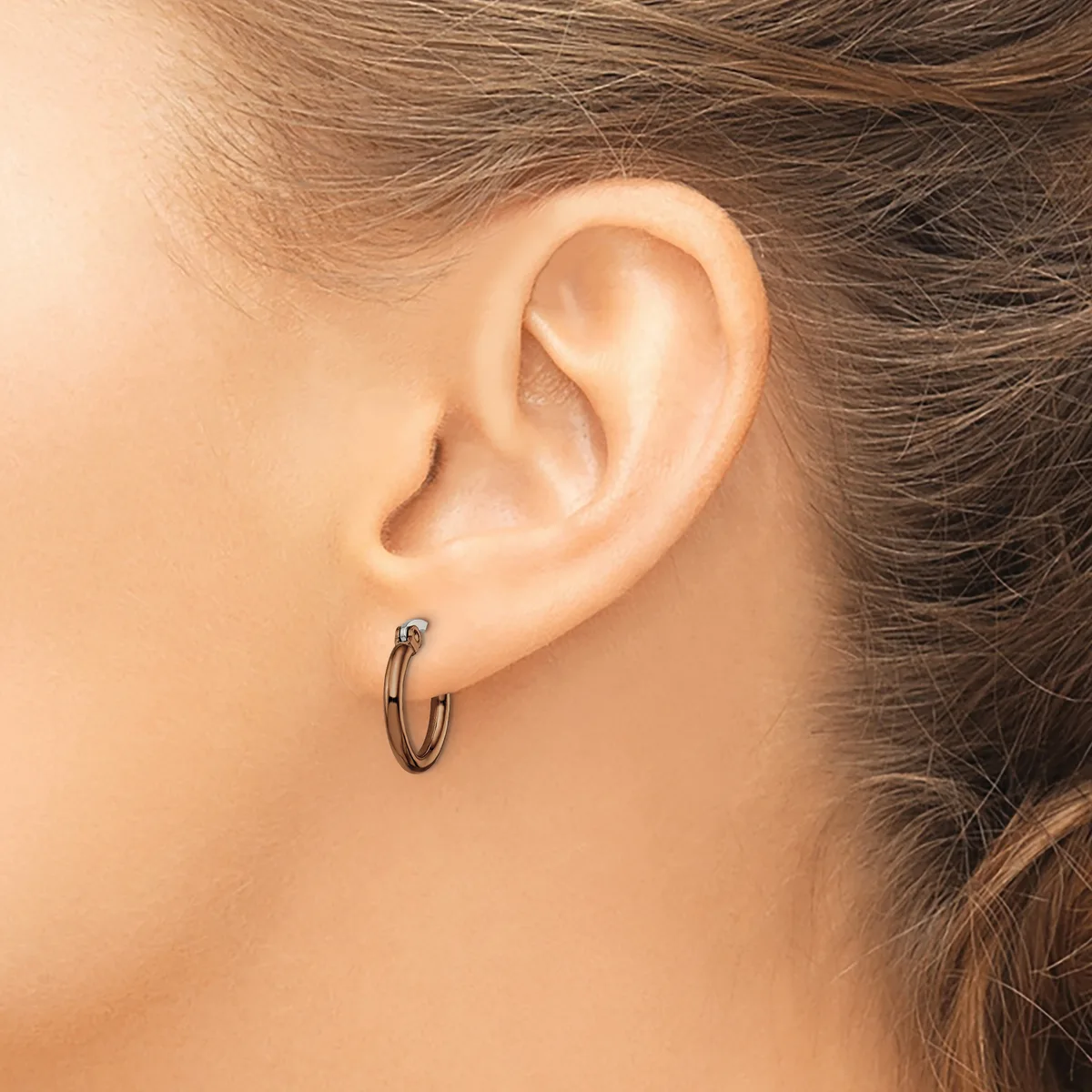 A person wearing a small dark metal hoop earring in their earlobe, shown in profile against their ear and neck.
