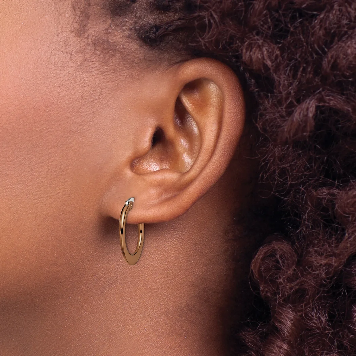 A person with brown skin and dark curly hair wears small gold hoop earrings in their earlobe, shown in profile view.