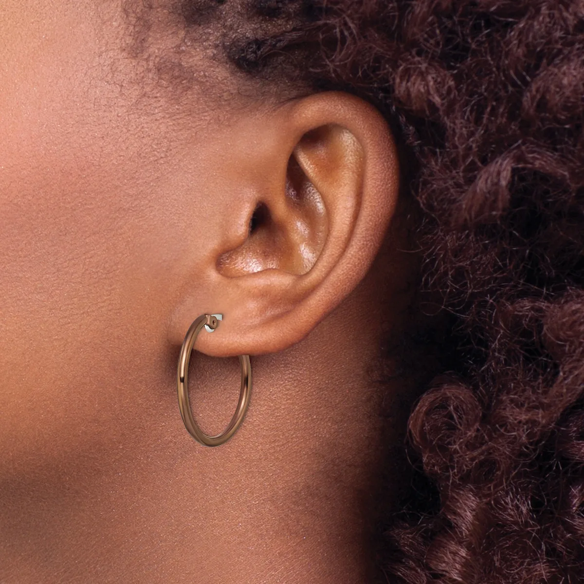 A person wearing a gold hoop earring in their earlobe, shown in profile with textured dark hair visible.