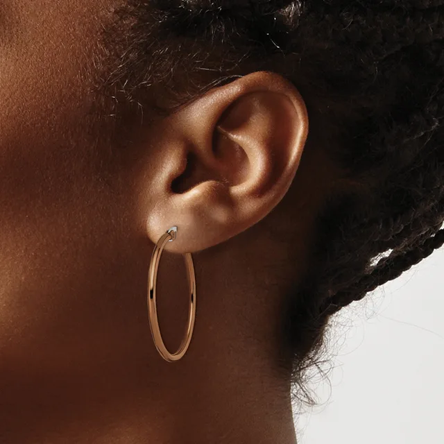 A person wearing a gold hoop earring, shown from the side profile of their face and ear against a neutral background.