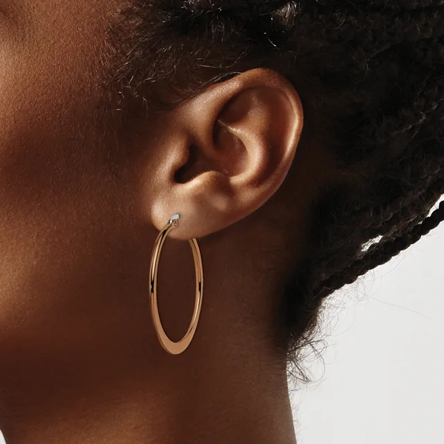 A person wearing a stud earring and large oval hoop earrings in rose gold, shown in profile against a light background.