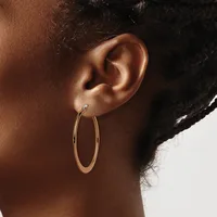 A person wearing a stud earring and large oval hoop earrings in rose gold, shown in profile against a light background.
