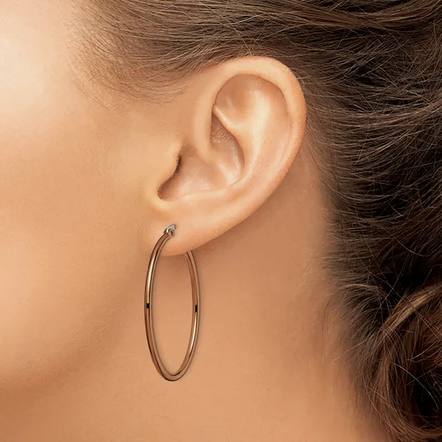 A person wearing simple oval hoop earrings with a polished metallic finish, shown from the side profile of their ear and neck.
