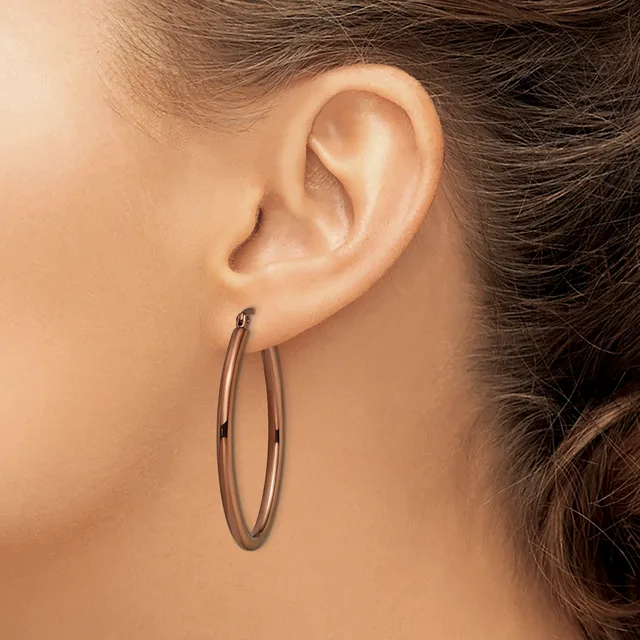 A person wearing a pair of polished oval hoop earrings in a rose or copper-toned metal, shown in profile view from behind.